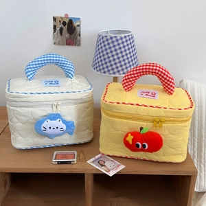 Detailed quilted makeup bag featuring heart stitching and plush fruit charms on a desk