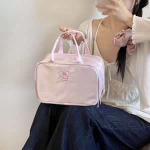 Detailed view of pink satin cosmetic bag featuring embroidered bow and dual handles