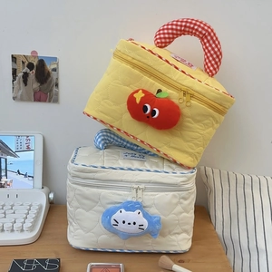 Close-up of quilted cosmetic bags with apple and cat charms on a wooden desk