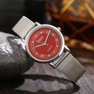 Detail of red dial quartz watch with Roman numerals and silver mesh band on stone base
