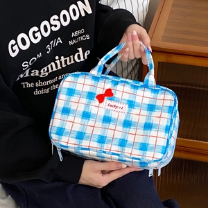Blue plaid makeup bag with red bow detail and dual zippers held by a person