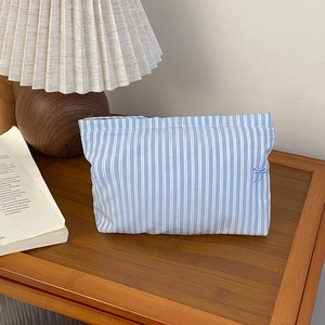 Detailed view of blue striped fabric makeup bag with cute decorative bows on a wooden desk