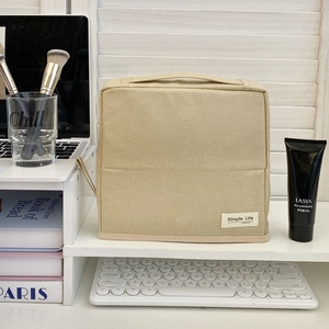 Standing beige fabric toiletry bag with handle on desk next to laptop and makeup brushes