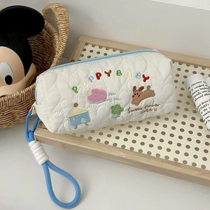 Detail view of white quilted pencil case with puppy embroidery and light blue zipper