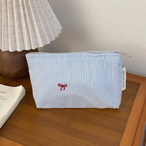 Close-up of blue striped travel pouch with red bow embroidery on a wooden surface