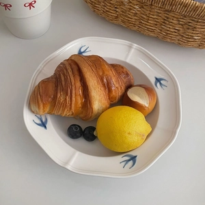 Detail view of a ceramic swallow plate featuring pastries and fruit in a rustic setting