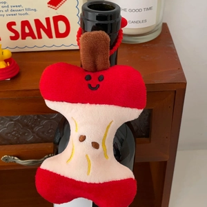Detailed view of apple core plush pendant with red beads hanging on a decorative bottle