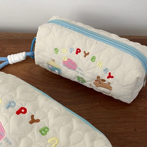 Detail of quilted heart texture and puppy embroidery on cream-colored cosmetic bag