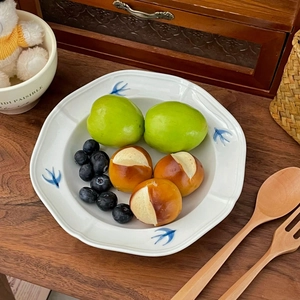 Detail of white ceramic plate with blue swallows holding small bread rolls and fruit
