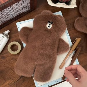 Detailed plush texture of a brown bear pencil case with stationery on a wooden desk