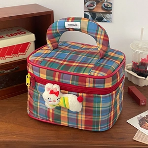 Close-up of a plaid makeup bag with wide handle and cute rabbit pendant on wooden desk