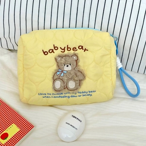 Detail of yellow quilted makeup bag with teddy bear embroidery and blue zipper closure