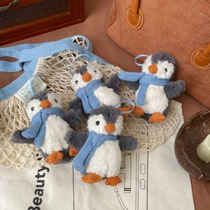 Detailed plush penguin keychains with blue scarves and grey-white fur on a warm background