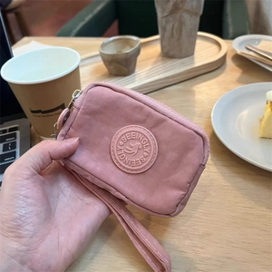 Portefeuille en nylon rose avec fermeture éclair et dragonne dans un café