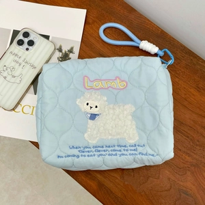 Detailed close-up of light blue quilted makeup bag with cute embroidered lamb and blue strap