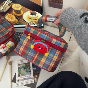 Detail of checkered makeup bag featuring a cute red plush charm and sturdy handle