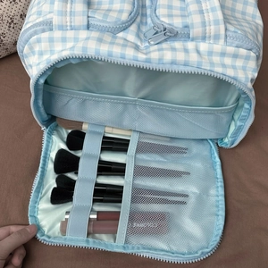 Close-up of blue gingham makeup bag interior showing elastic brush slots and mesh pocket
