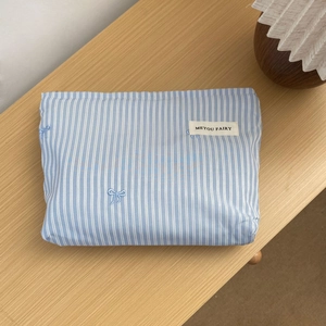 Detail of blue striped makeup bag with embroidered bow on a wooden surface