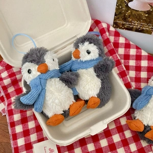 Cute plush penguin keychain with blue scarf in a rustic picnic basket setup