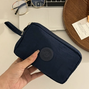 Détail d'une pochette en nylon bleu marine à trois zips avec un patch de marque rond