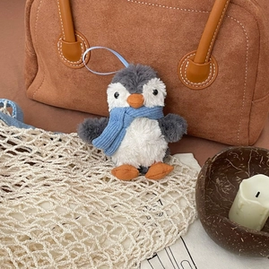 Detail of cute plush penguin pendant featuring a blue knit scarf on a stylish brown bag
