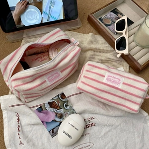 Pink and white striped terry cloth cosmetic bags on a wooden tray with sunglasses