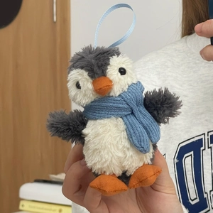 Close-up of cute plush penguin charm with blue scarf and orange feet on blue lanyard