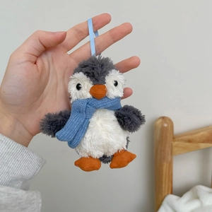 Close-up of cute plush penguin keychain with blue knitted scarf and silk hanging loop