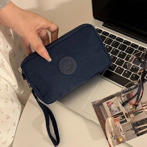 Détail d'une pochette en tissu bleu marine avec logo tenue près d'un ordinateur