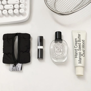 Flat lay of a black puffer mini coin pouch with zipper and stylish lifestyle accessories