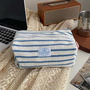 Detailed view of a blue and white striped terry cloth makeup bag with top zipper and woven label
