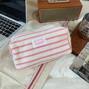 Detailed view of pink striped terry cloth makeup bag with Jolly House logo on a desk
