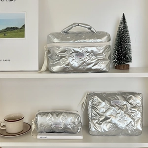 Quilted silver toiletry bag set with bow patterns shown in a minimalist room setting