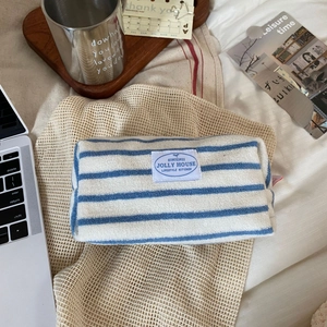Detail of blue and white striped terry cloth cosmetic bag with logo on a wooden tray