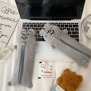 Close-up of two grey plush animal pencil cases on a minimalist desk with office supplies