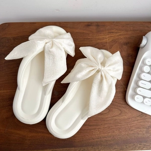 Chic white silk bow flip flops with soft EVA sole on a wooden desk with keyboard