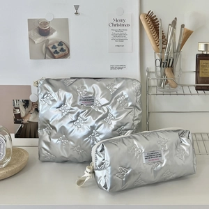 Silver quilted makeup bag set with bow pattern and metal finish on a white desk