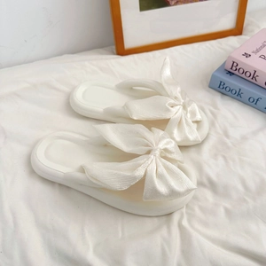 Detail of a creamy white flip flop featuring a pearlescent fabric bow on a soft sole
