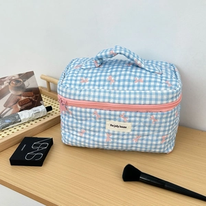 Close-up of blue checkered quilted makeup bag with pink bow accents and logo tag