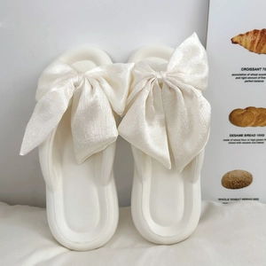 Close-up of white flip-flops with large silk bow detail and soft sole texture