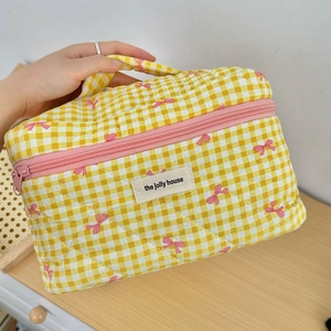 Detailed macro view of yellow checkered quilted cosmetic bag with pink bows and handles
