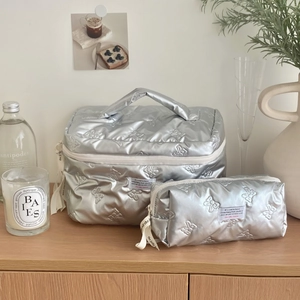 Close-up of silver quilted makeup bags with bow texture and metallic finish on wood table