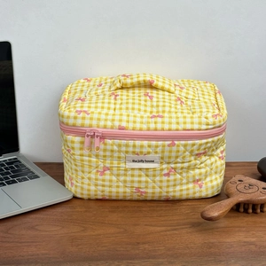 Detailed quilted texture of yellow plaid makeup bag with pink bow prints and double zippers