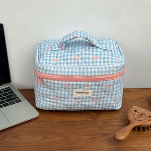 Blue gingham quilted makeup bag with pink bow accents and top handle on a desk