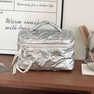 Detailed view of silver quilted makeup bag with butterfly pattern and top handle