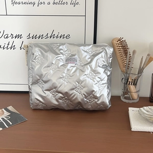 Macro shot of silver quilted cosmetic bag featuring textured bow patterns and brand label