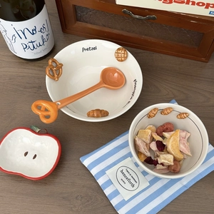 Close-up of ceramic bowls with relief bread patterns and a pretzel-shaped spoon on a wooden table