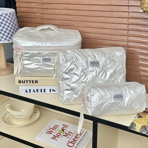 Three-piece set of white quilted cosmetic bags with bow patterns in home setting