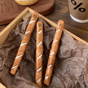 Close-up of baguette-shaped ceramic coffee stirrers with smiley faces in a wooden box