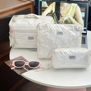 Three-piece set of white quilted cosmetic bags with bow stitching and ribbon zipper detail